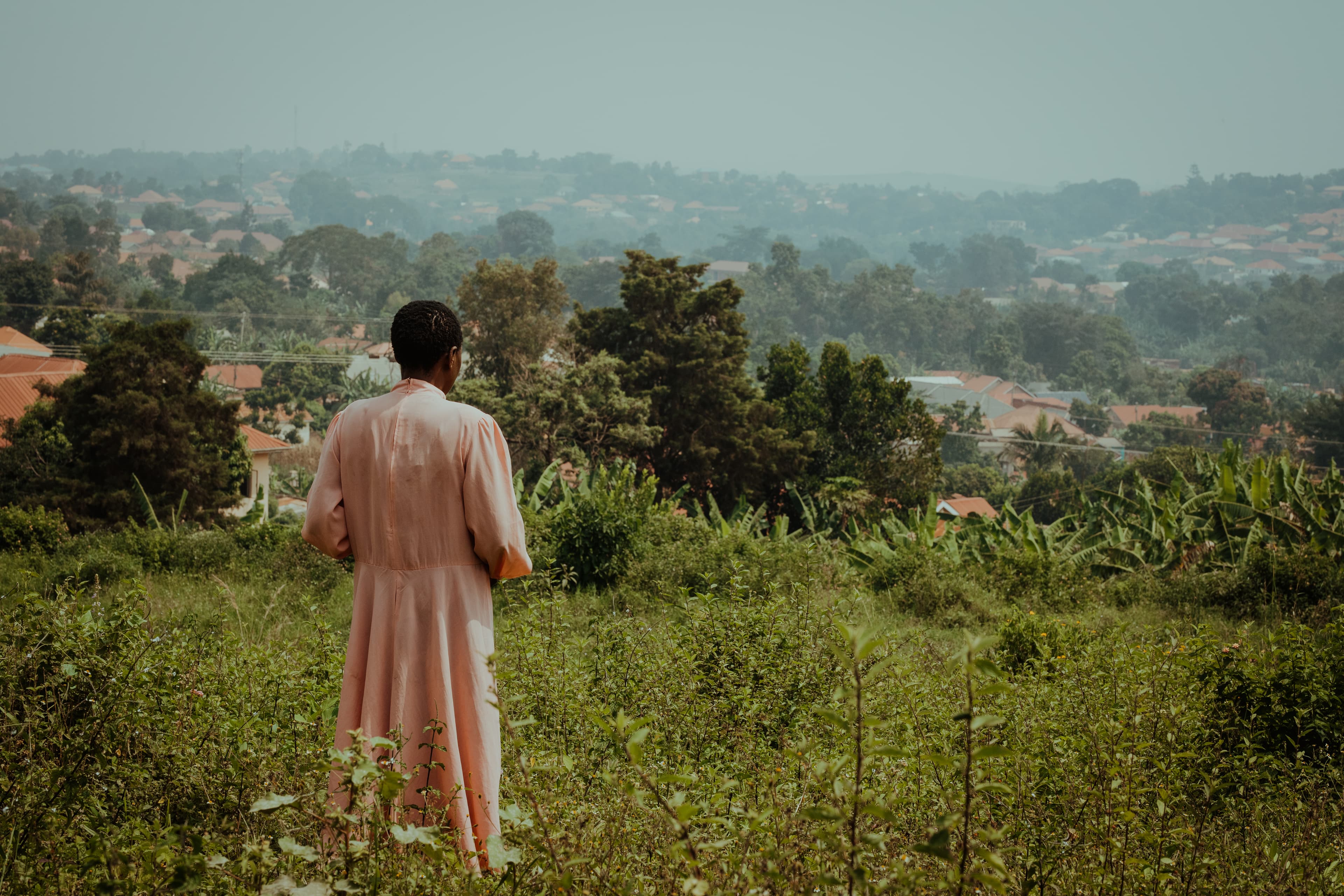 A woman stands in a field while looking toward the landscape.
