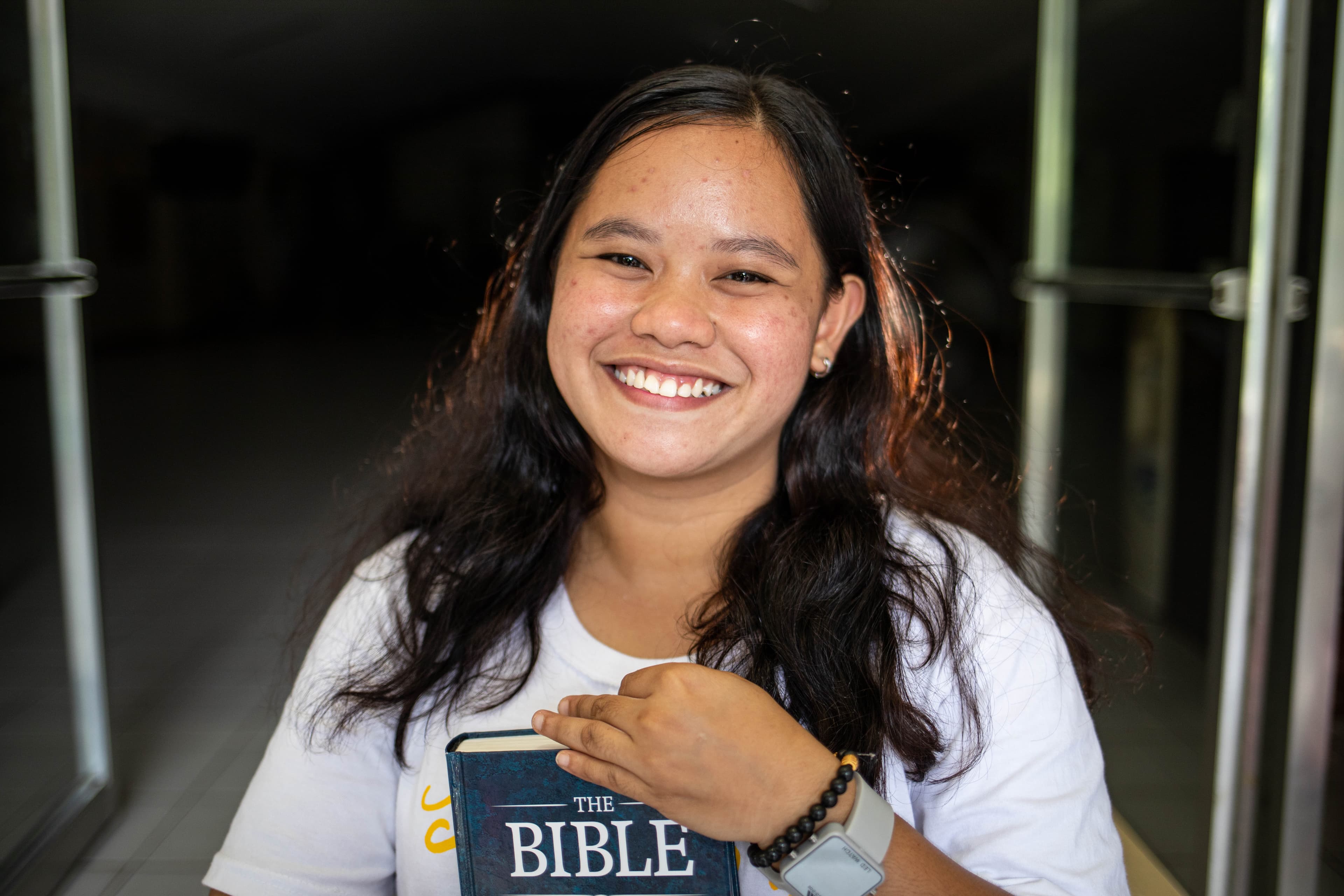 A young girl holds a Bible while smiling for the camera.