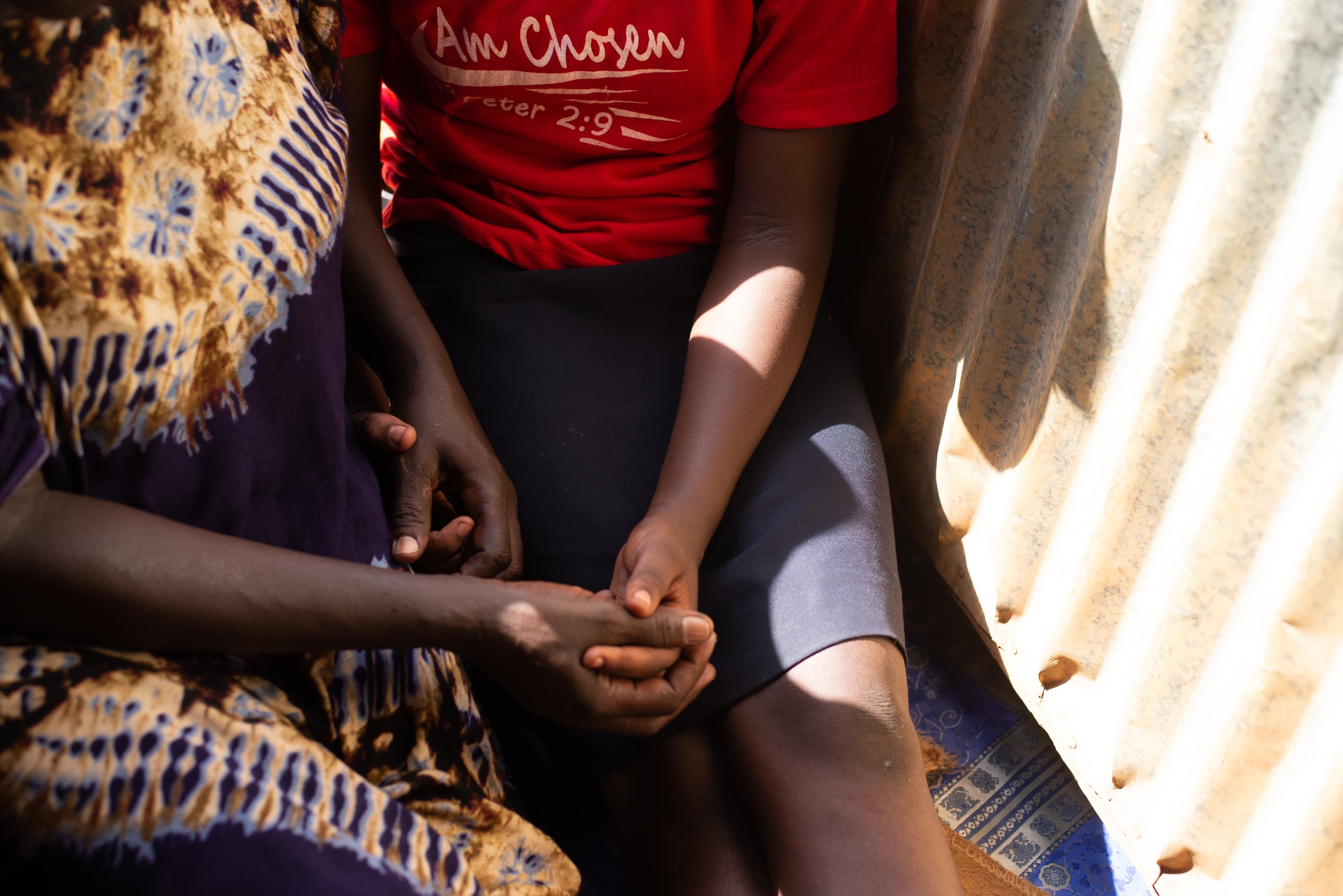 A mother and son sit on the floor holding hands.
