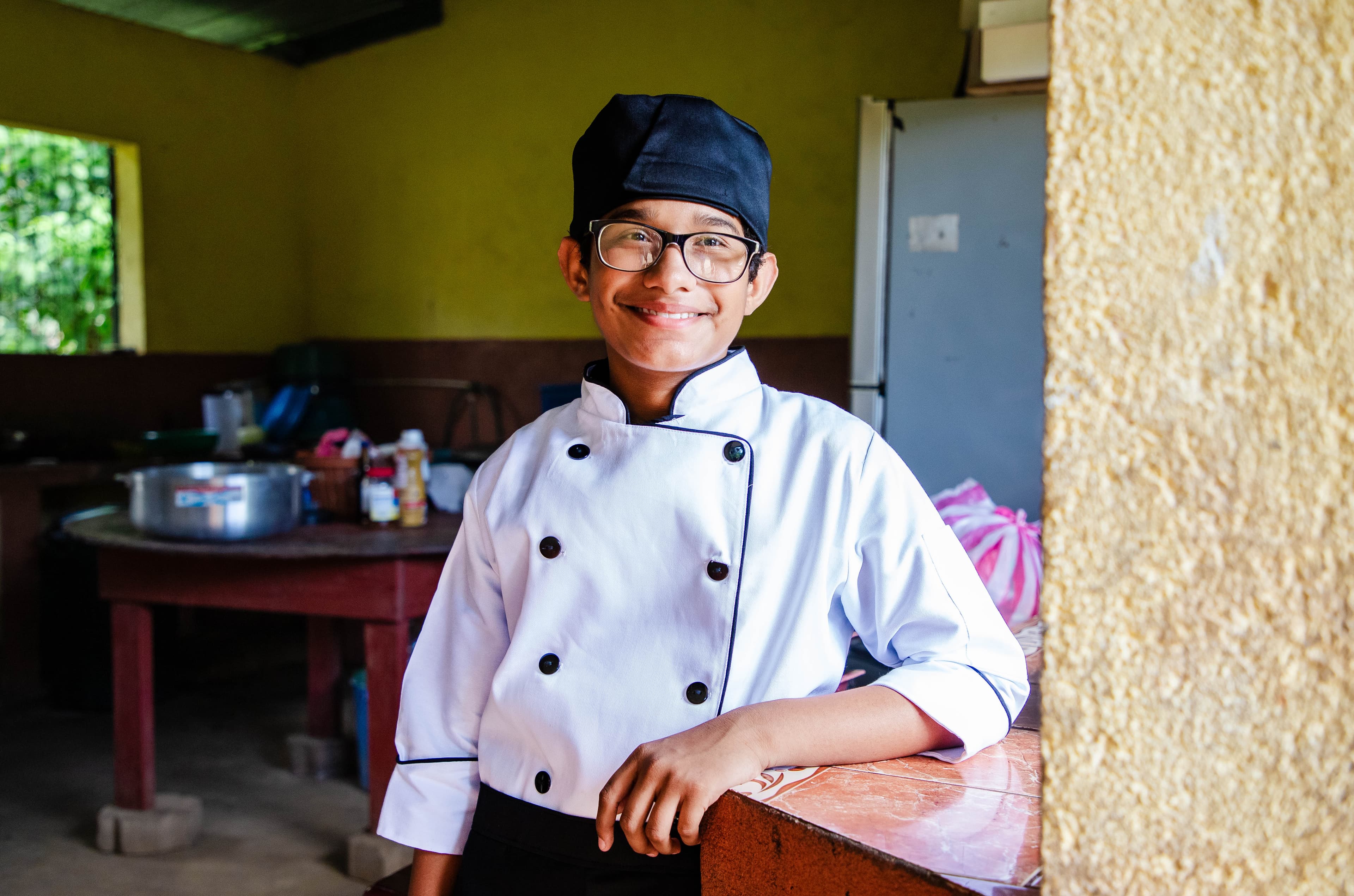 A young boy wearing a chef’s uniform smiles for the camera.