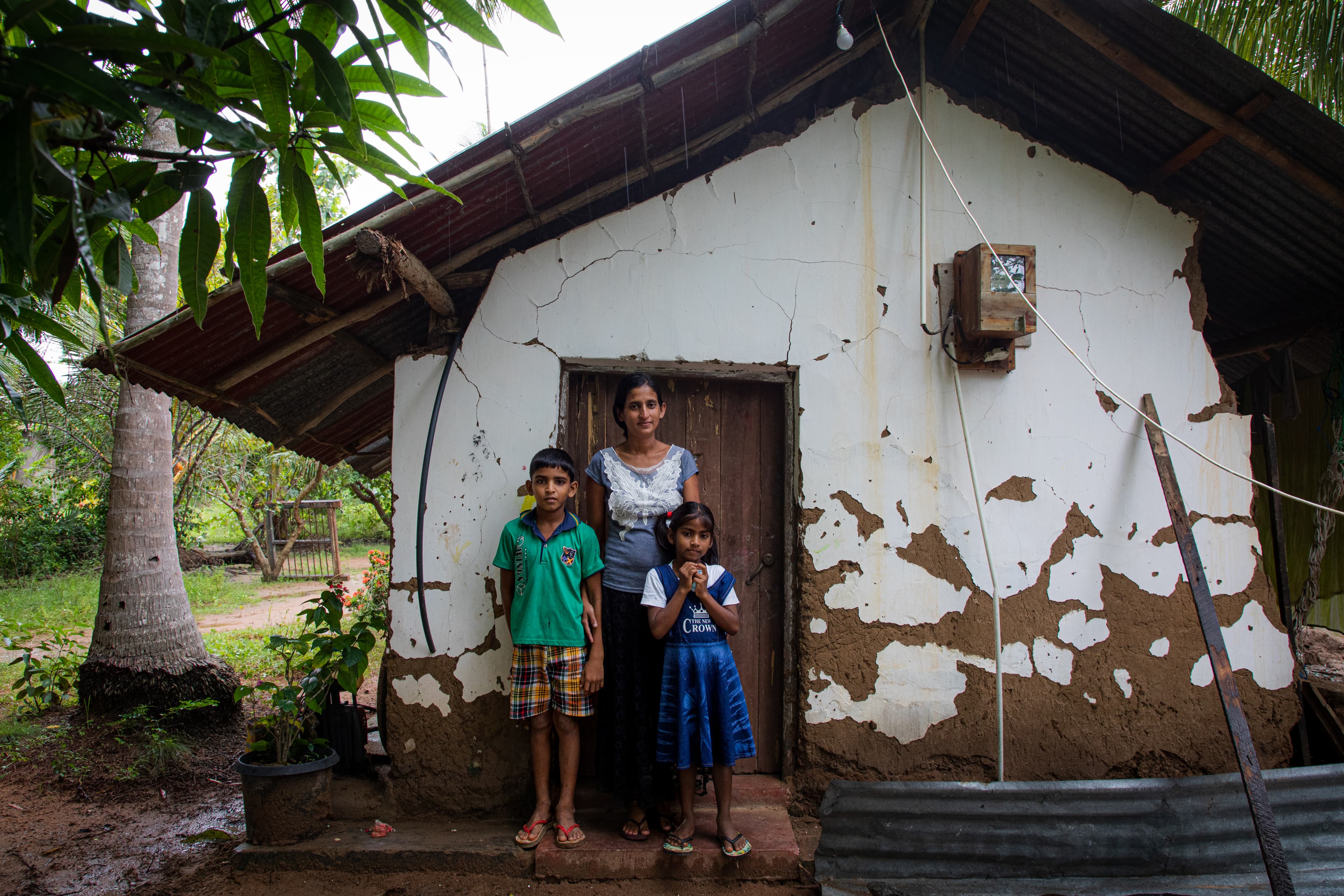 A mother stands with her son and daughter in front of their damaged home.