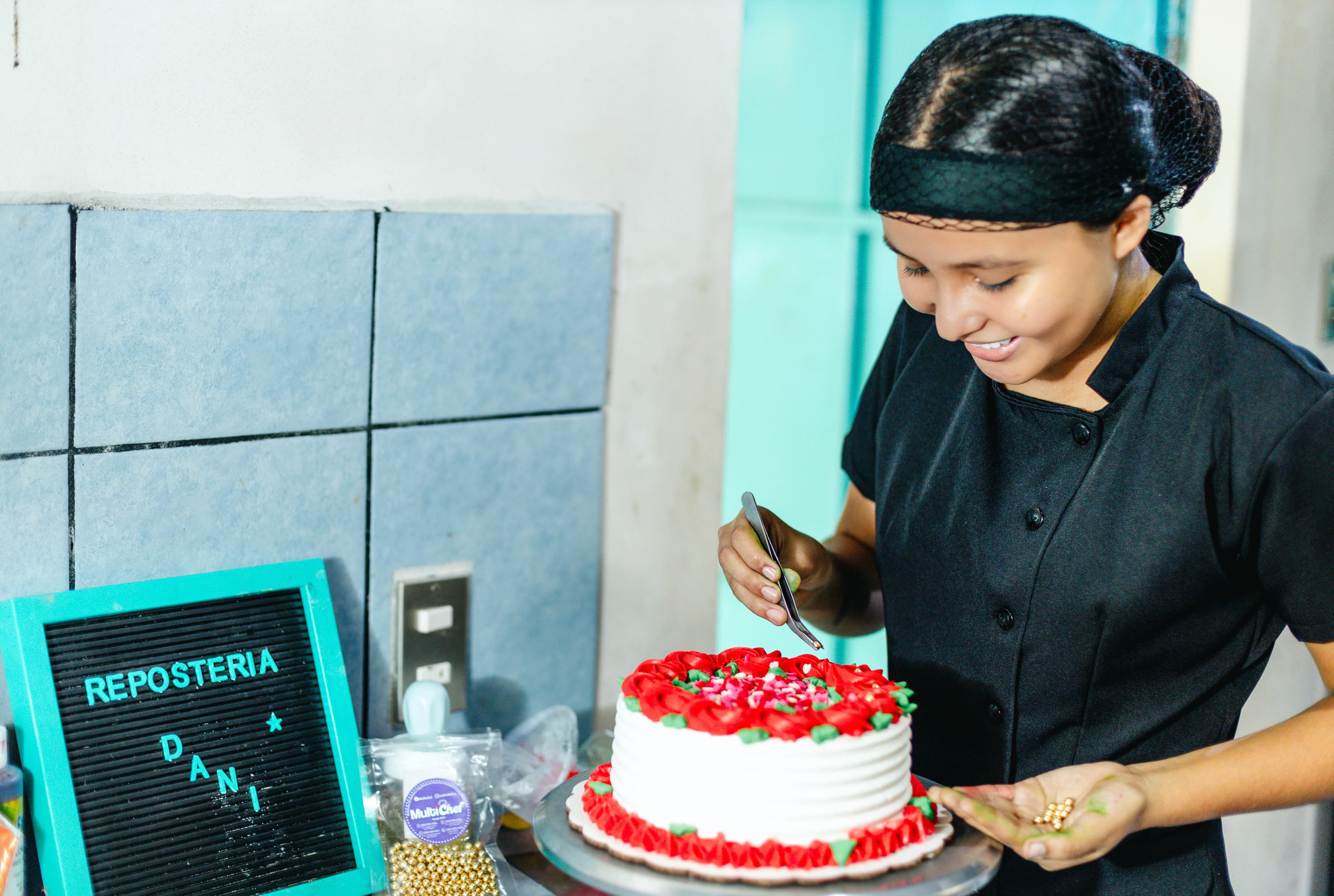A teen girl wearing a black chef's coat cuts a cake while smiling.