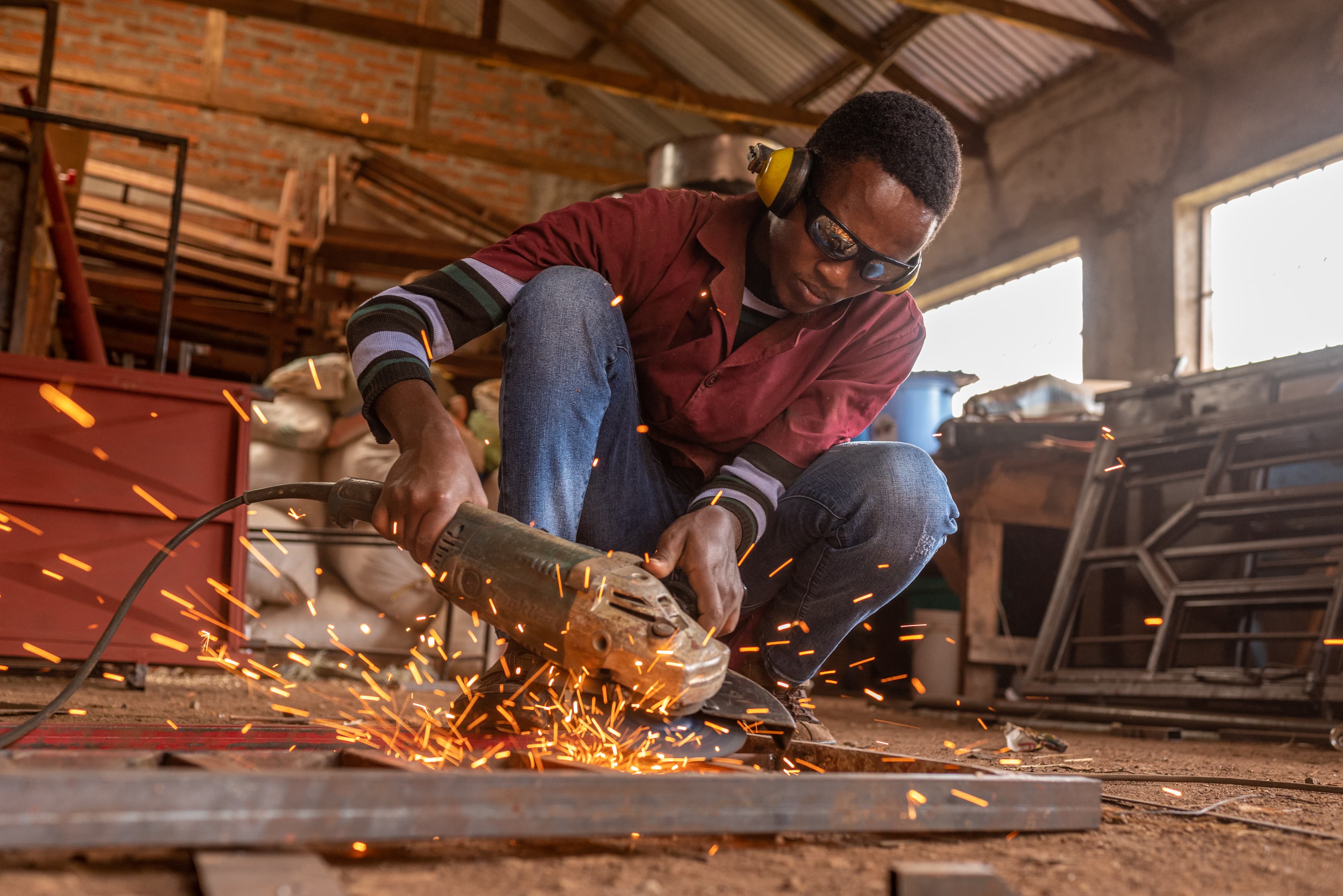 A welder wearing goggles works on a piece of metal while sparks fly.
