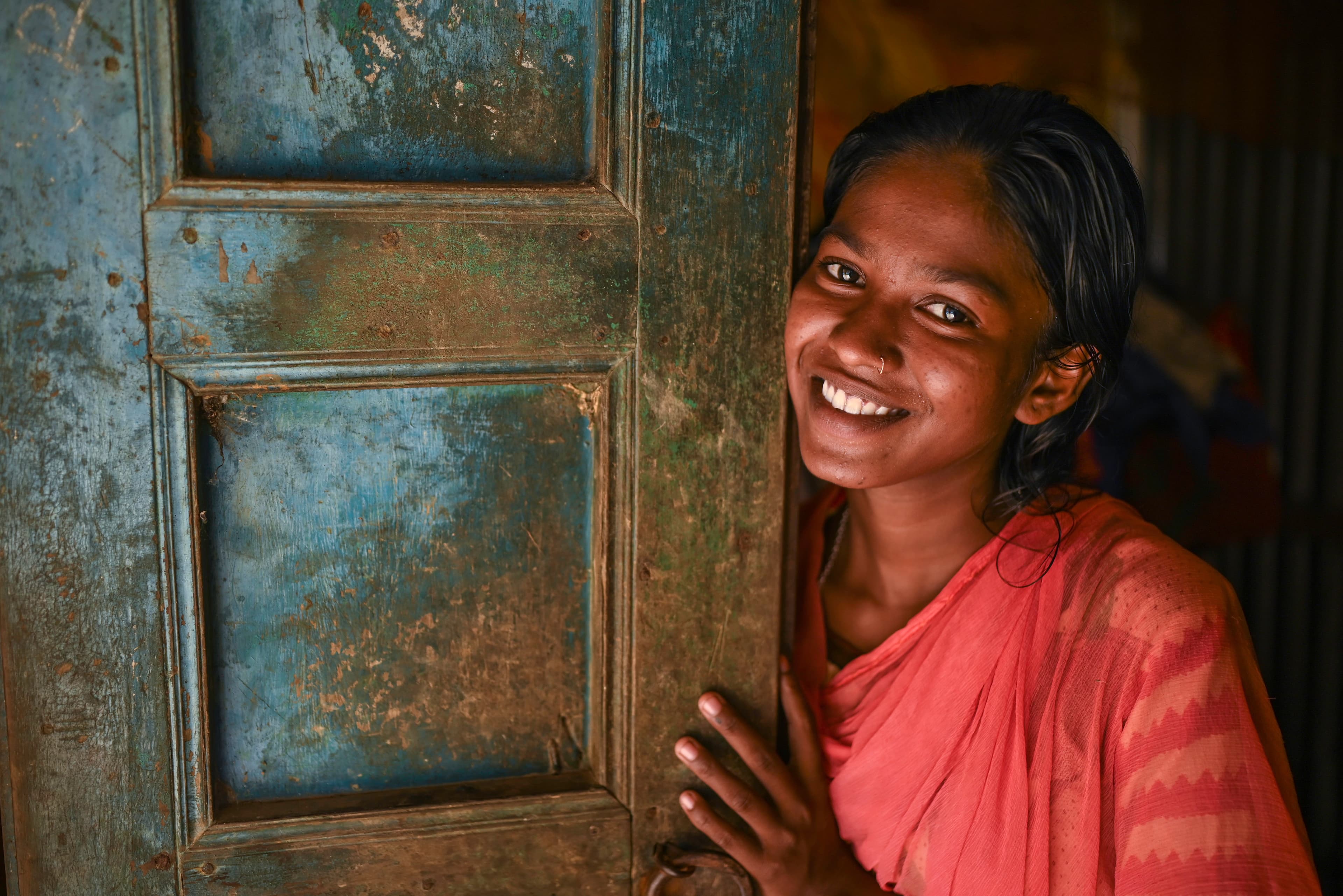 A teen girl leans against a door while smiling for the camera.