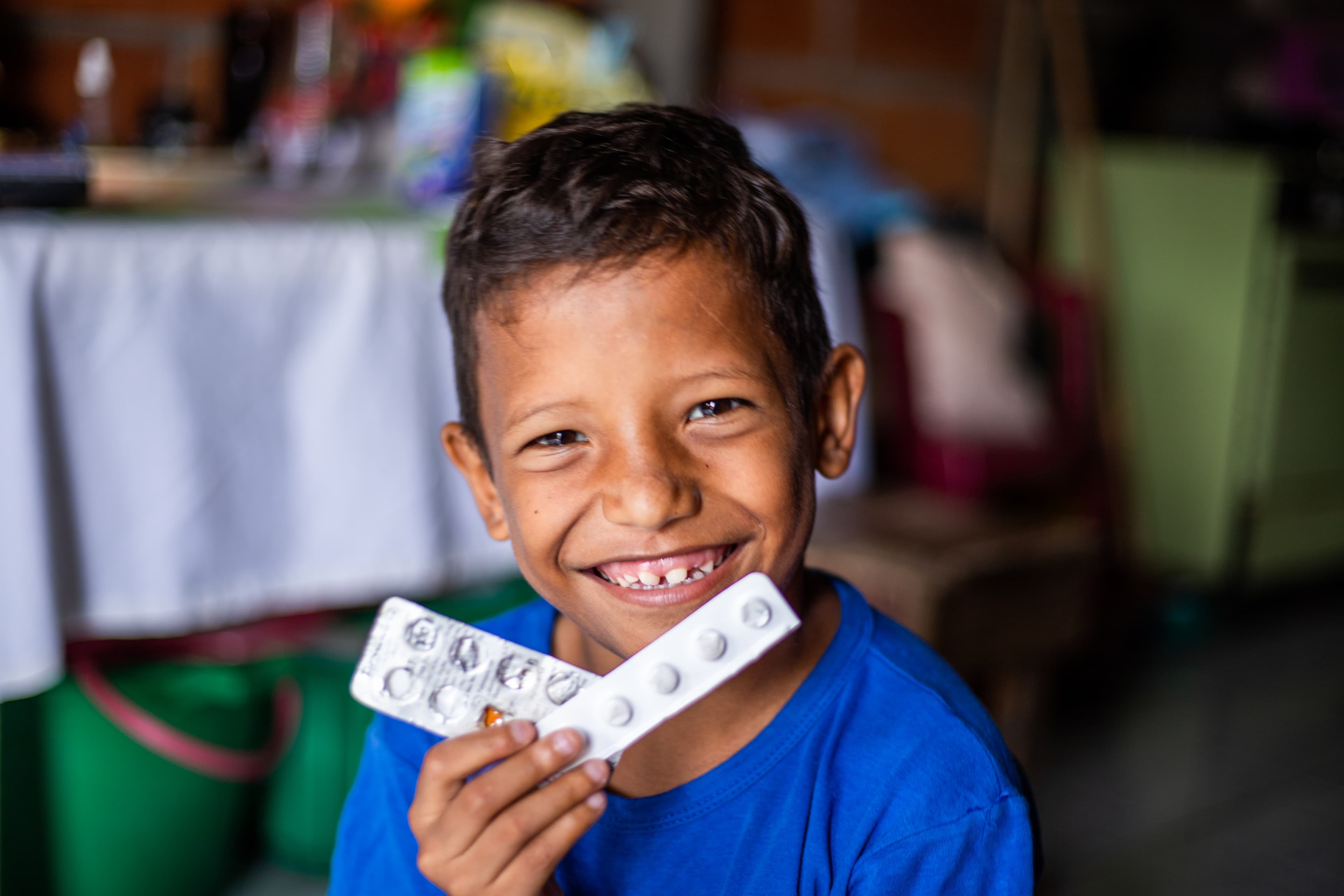 Boy in blue shirt smiles big, holding medication.