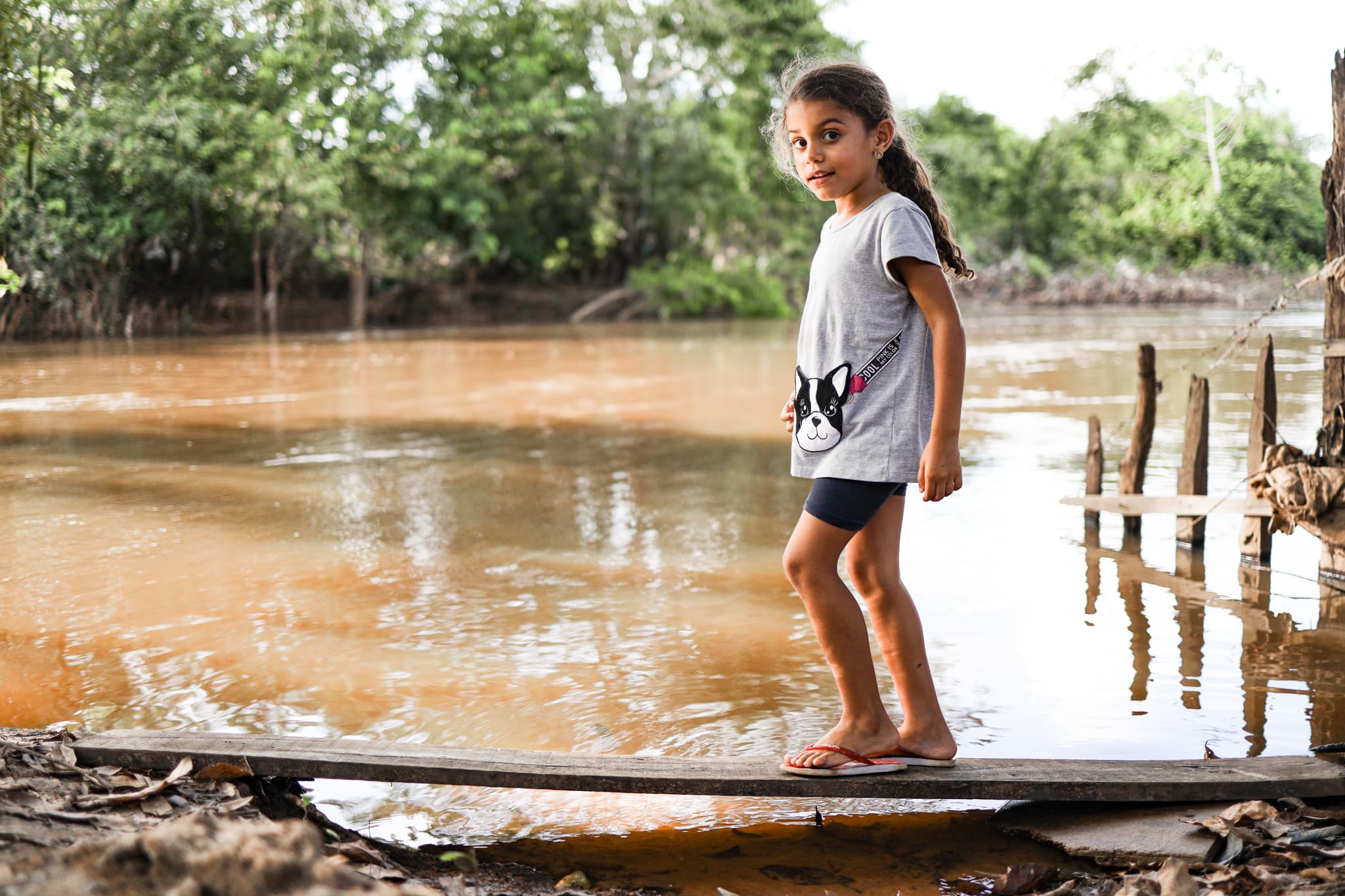 A young girl walks on a wooden plank over water.
