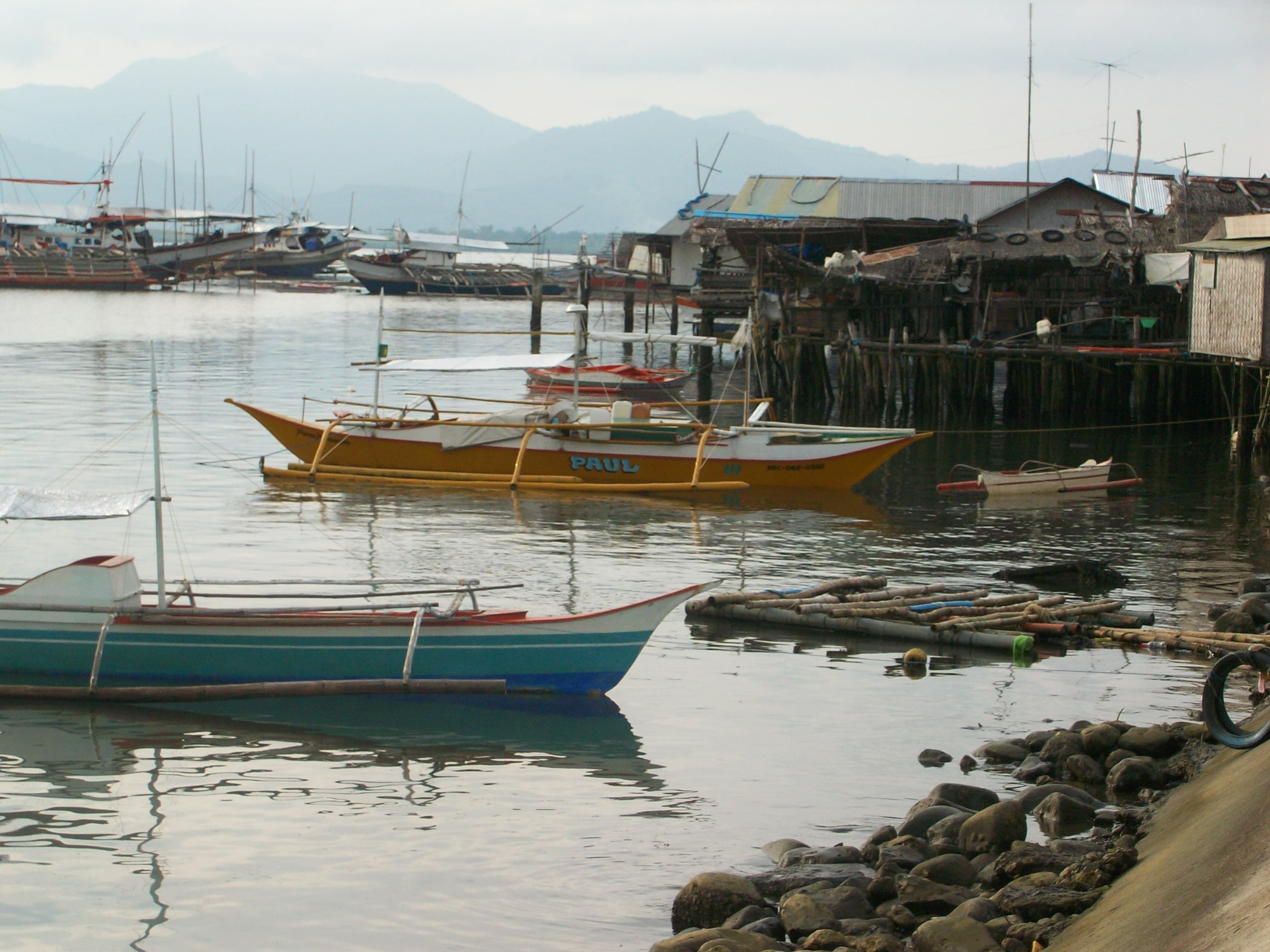 Boats float on a lake with buildings and mountains in the background.