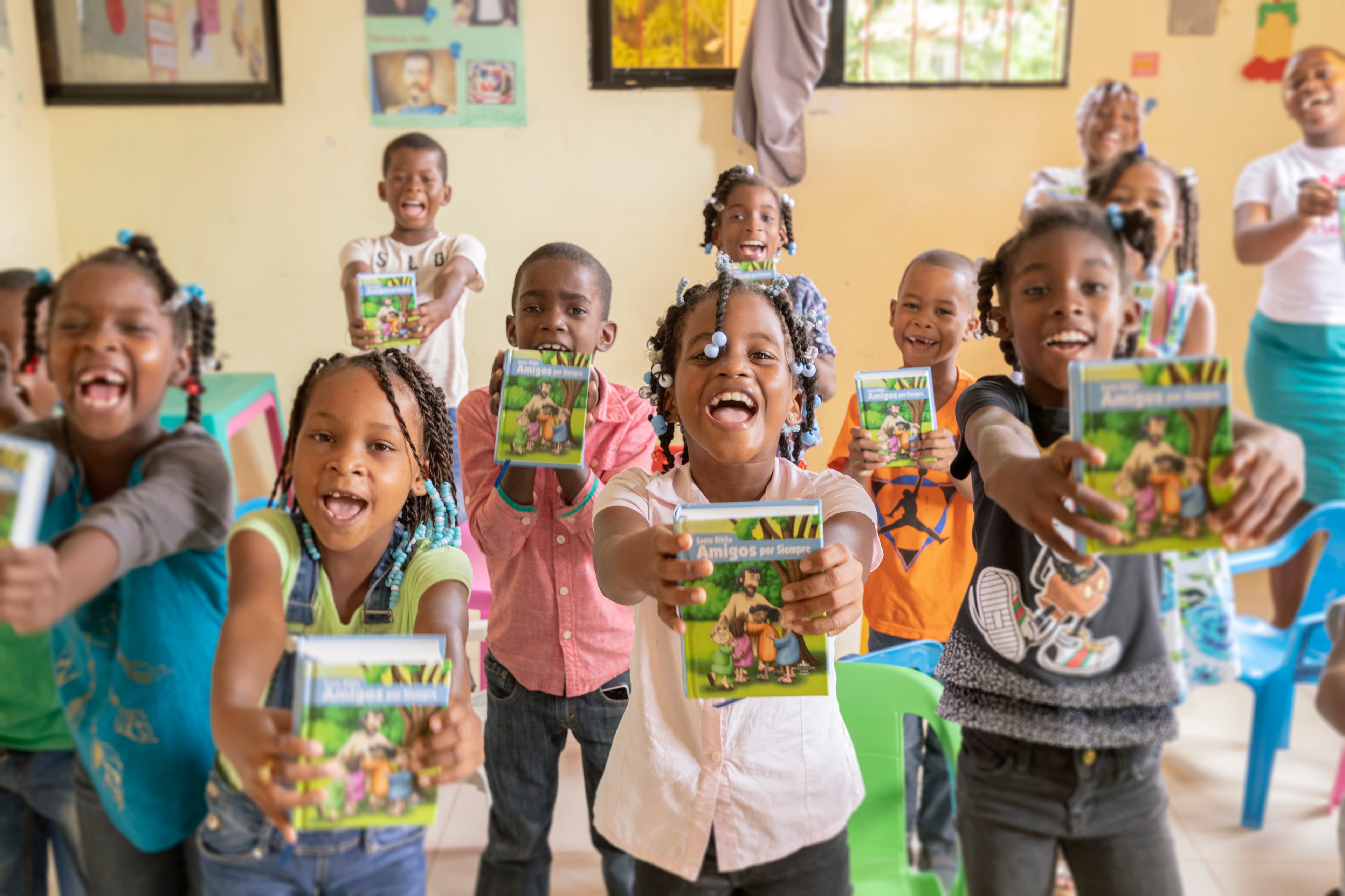 A group of children smile widely as they hold children's Bibles.