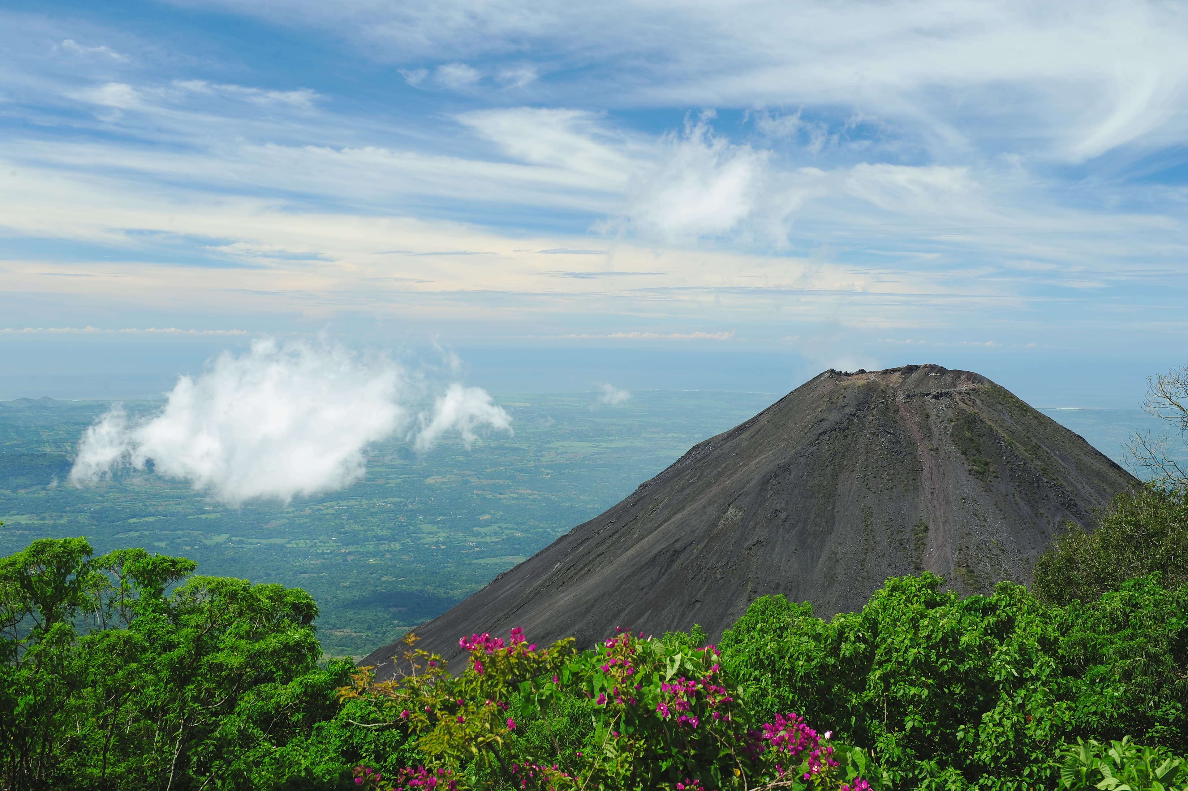 A volcano in front of a bright blue sky with clouds.