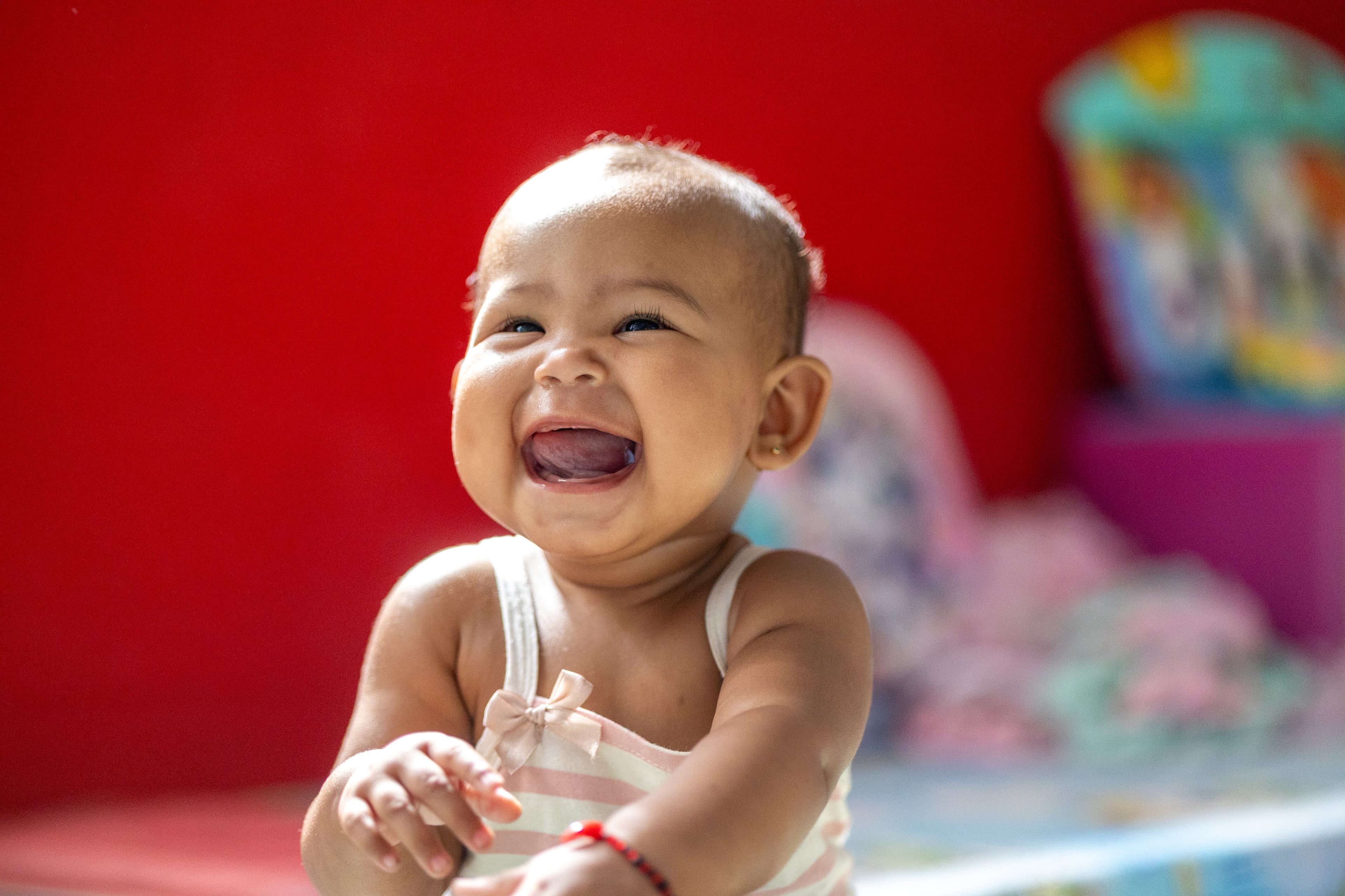 A baby girl wearing a pink and white striped shirt smiles brightly for the camera.