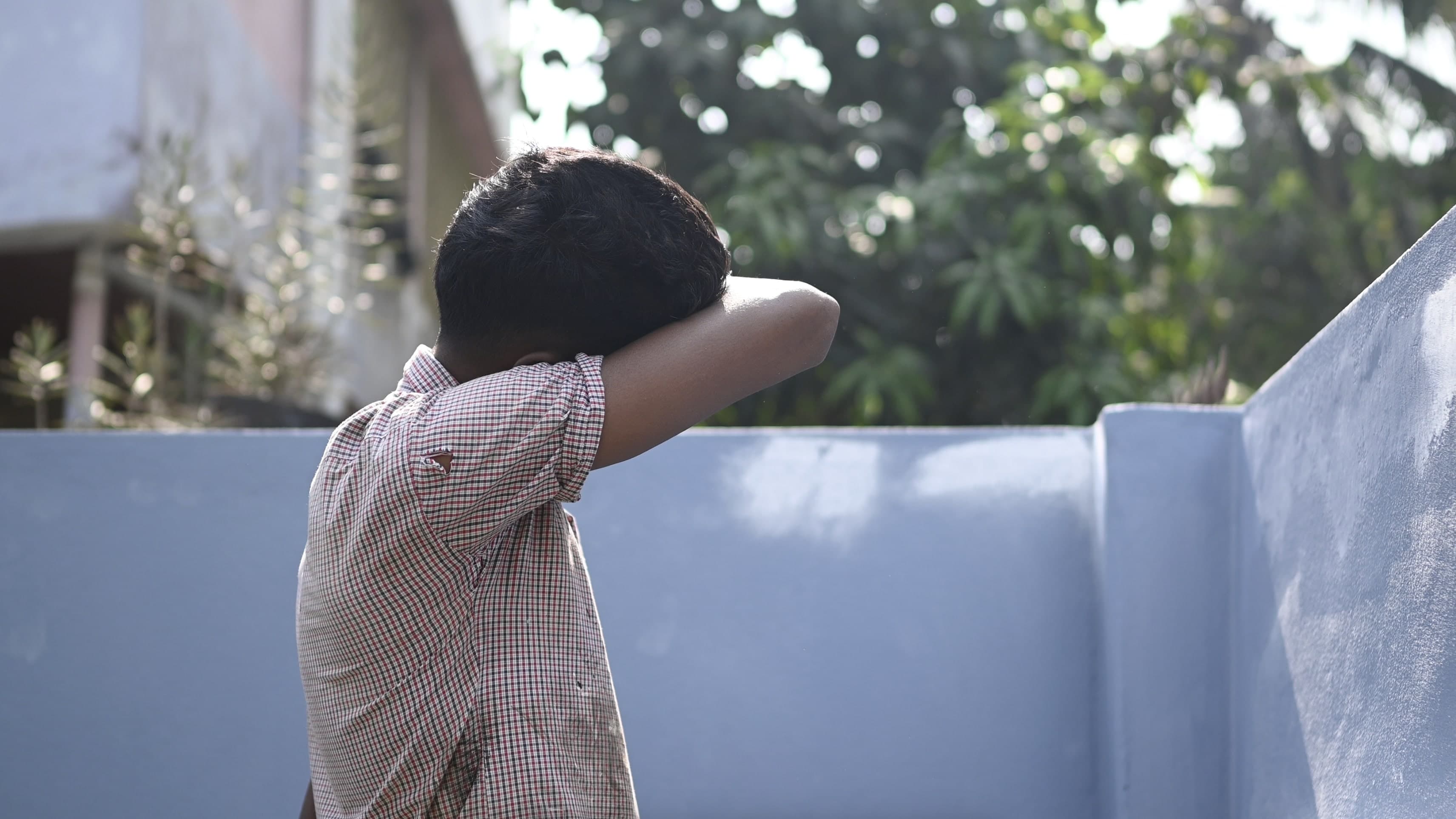 A young boy covers his face with his arm.
