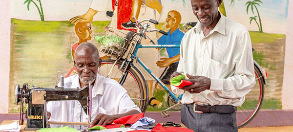 Two men sewing in front of a colorful mural