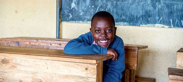 A boy sits at a school desk smiling