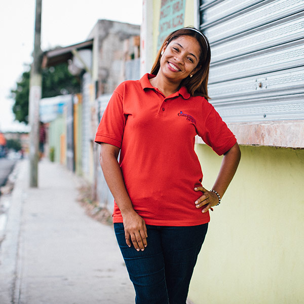 a woman in a red shirt stands with her head tilted