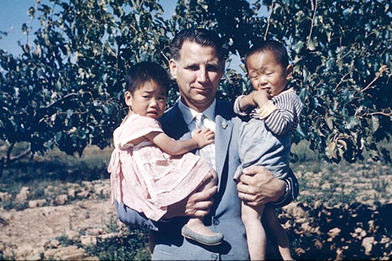 Rev. Everett Swanson holding two orphans in his arms.