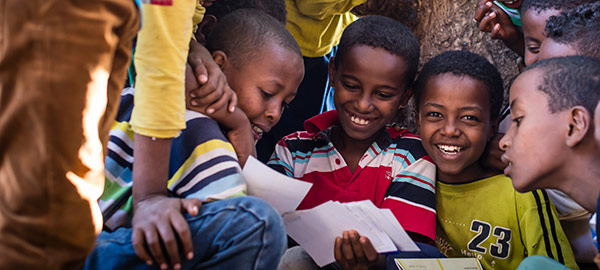 A smiling boy sits in a group of boys straining to read a sponsor letter one boy is holding