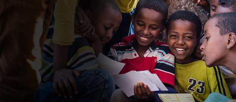 A smiling boy in a group of boys straining to read a letter from a sponsor