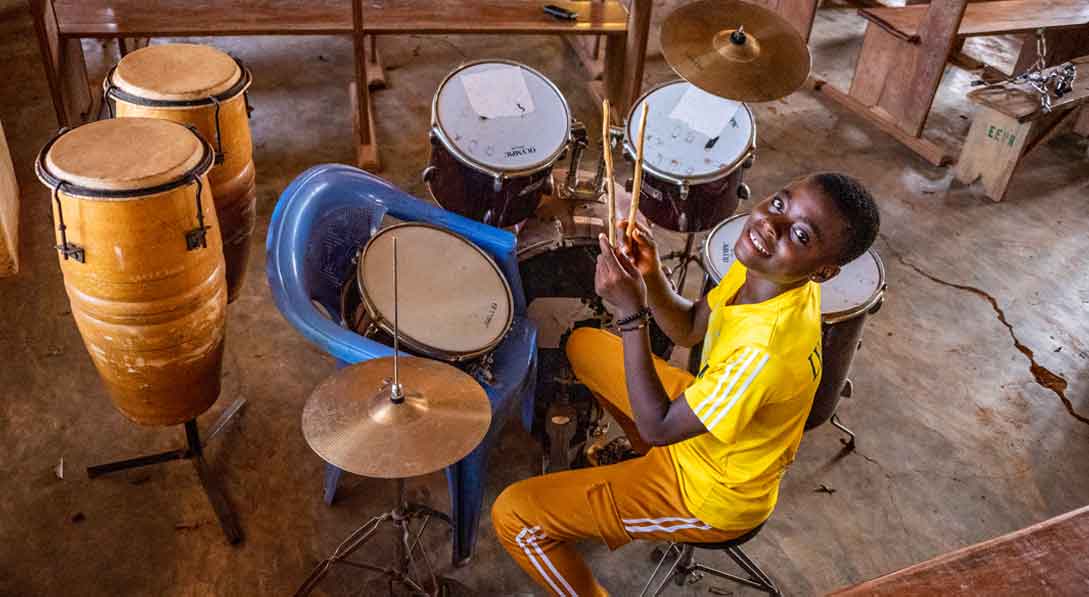 Reine dressed in all yellow sits in front of a drum set