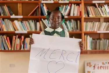 School girl holds sign that reads 'Merci' 
