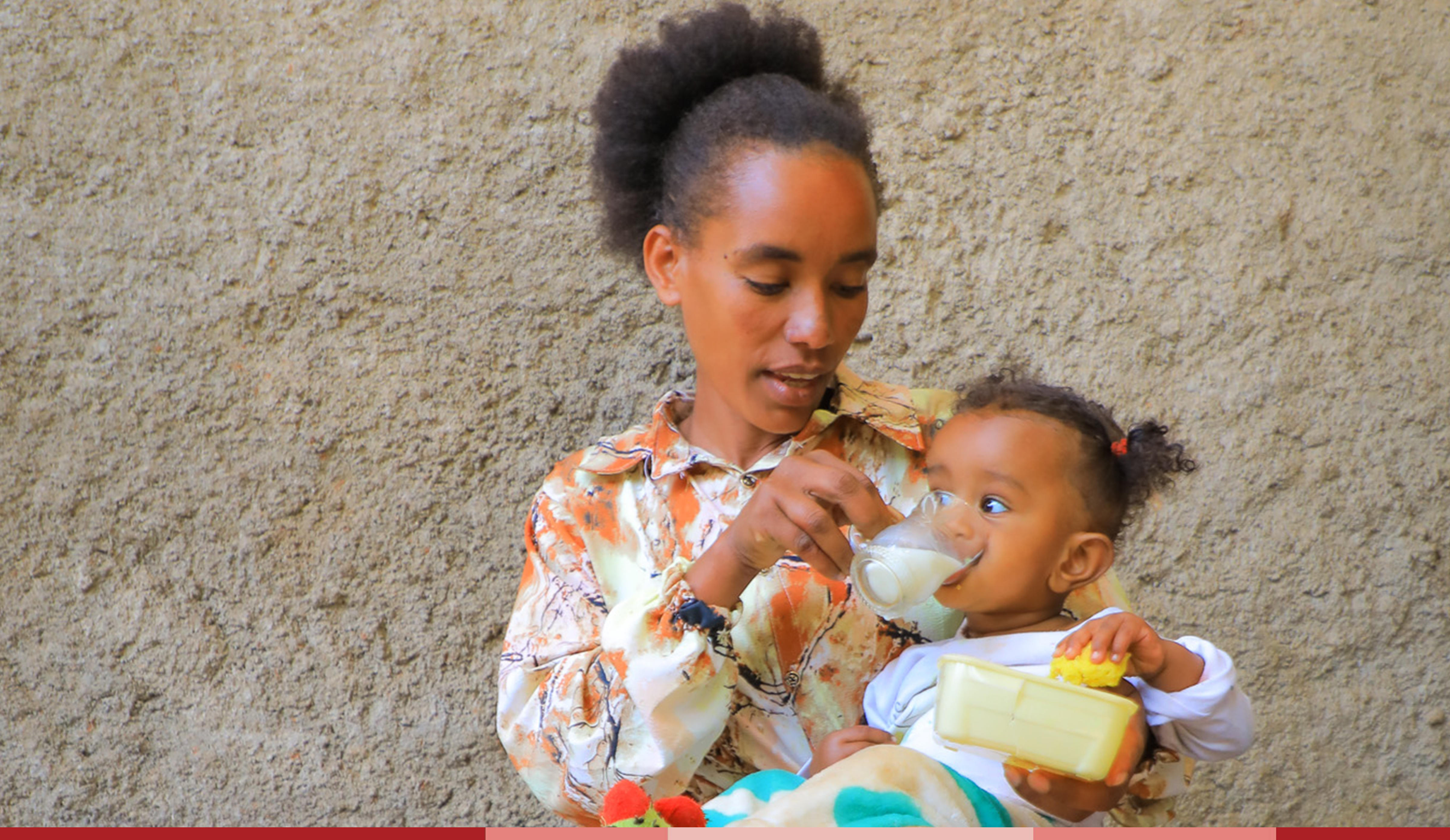 Ididiya sips from a cup of milk while being held by her mom