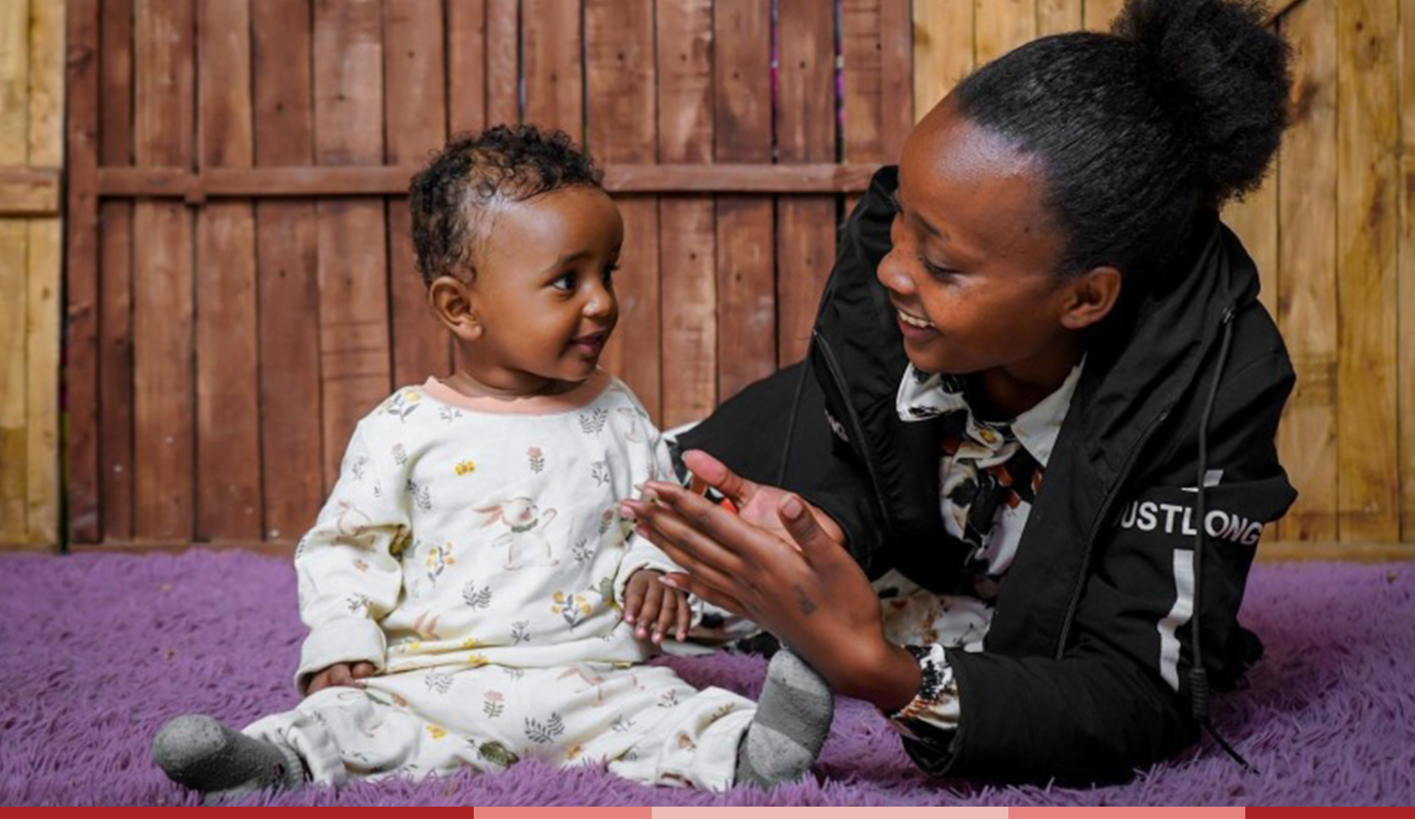 Zertihun plays with baby Barnabas who is sitting up and smiling