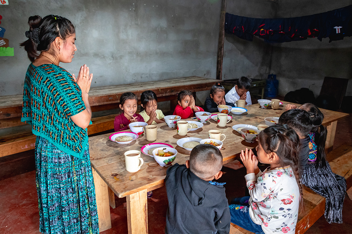 Woman stands and prays at table with children