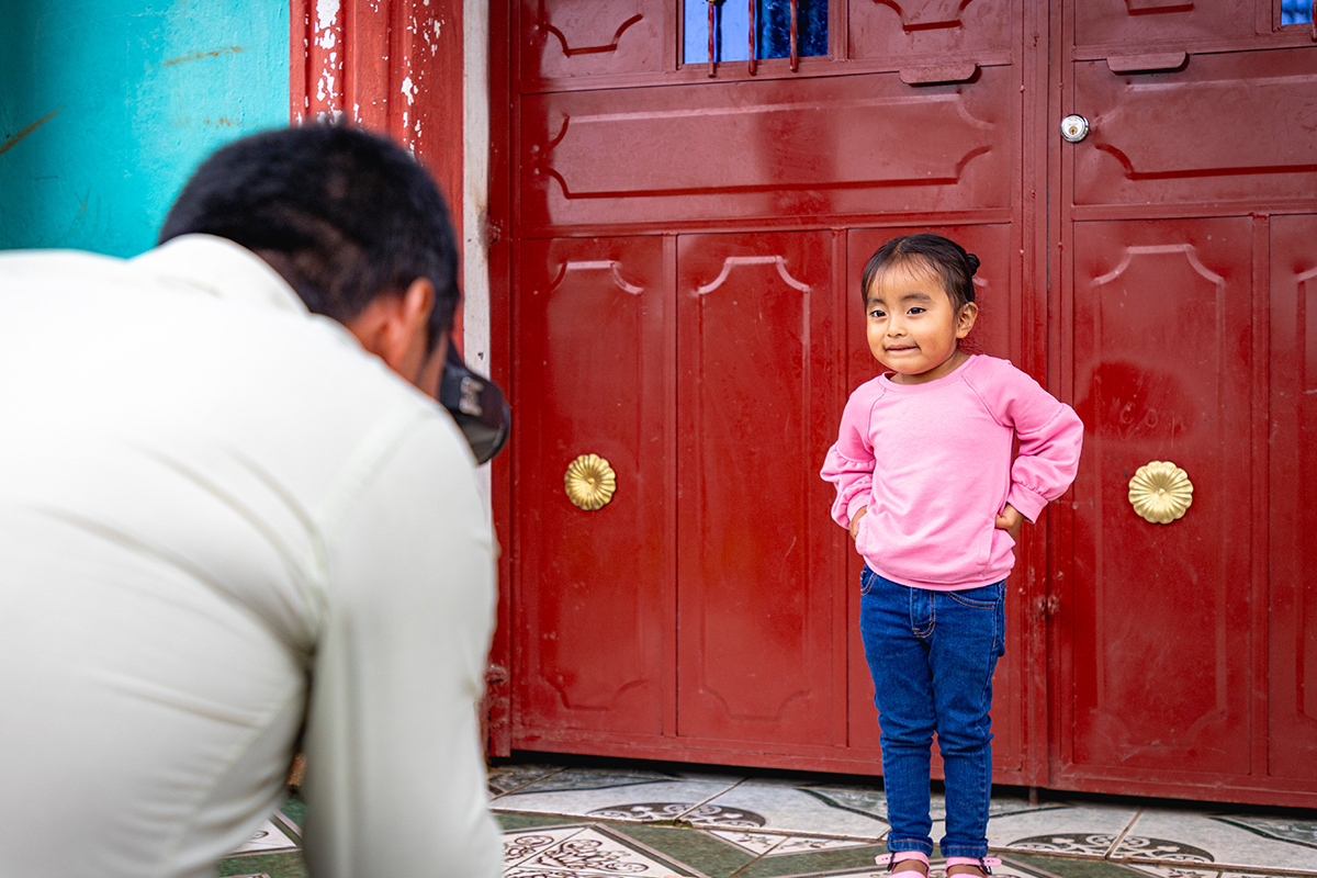 Little girl in pink shirt poses in front of red background for photo
