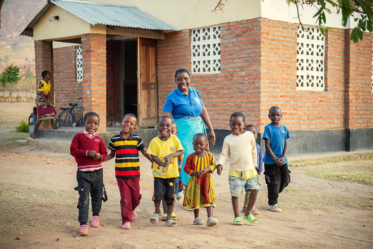 children standing and smiling in front of their Malawi FCP center.