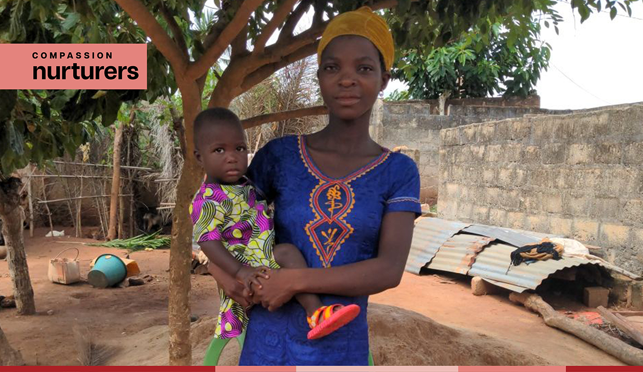 Agbessinou stands under a tree and holds her baby
