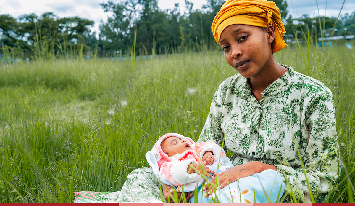 Zertihun holds her newborn baby while sitting in a lush green field
