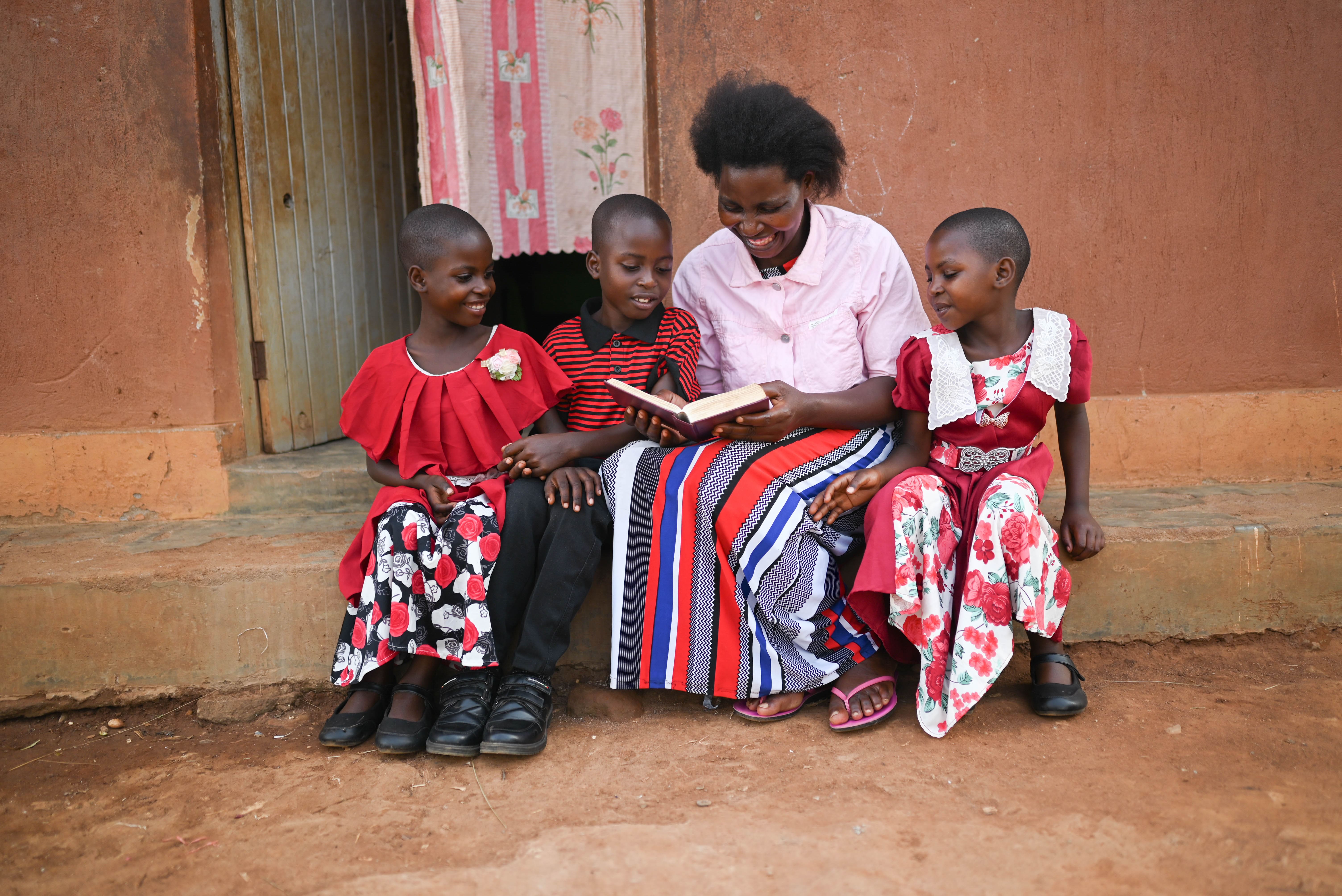 A woman site with three children as she reads the Bible to them.