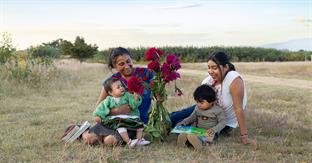 Mothers sit with their children on the grass and hold flowers.