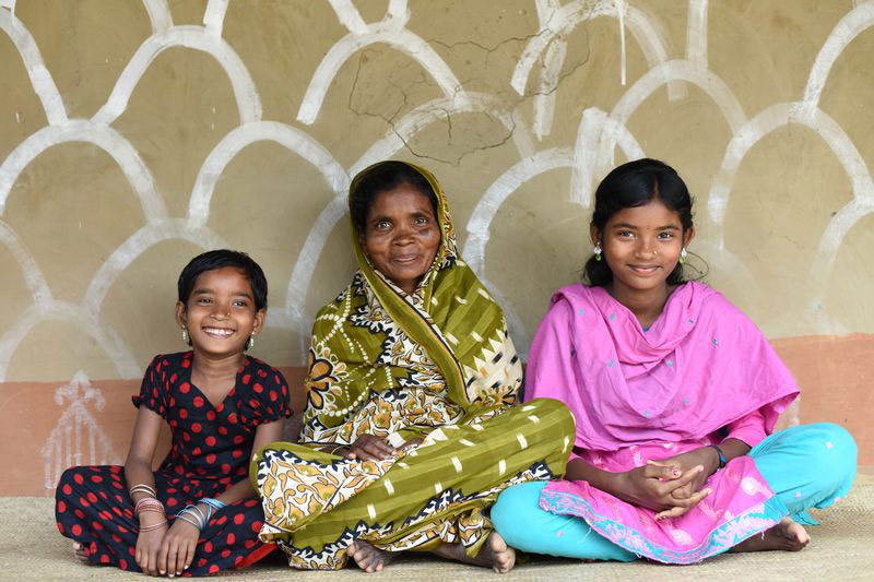 Two young girls sit on the ground next to their mother