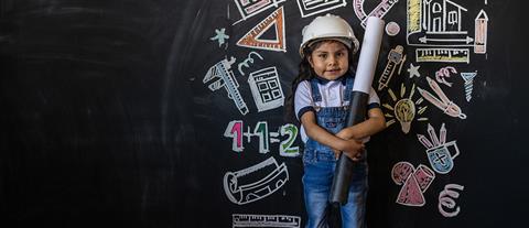young girl dressed as a contractor stands in front of a chalkboard