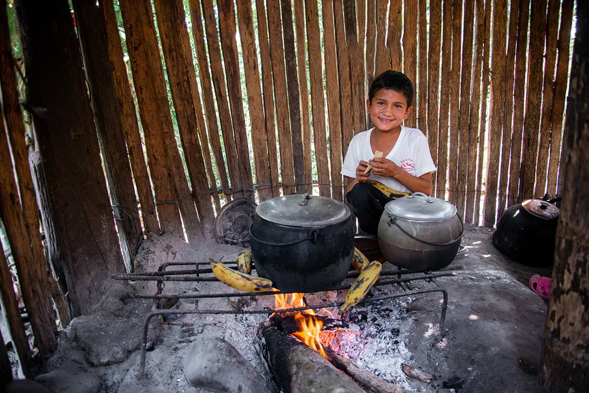 Boy sitting by a cooking fire with pots on a grate