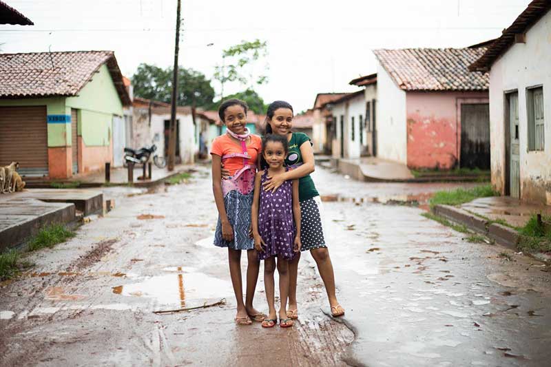 A girl who received help to fight scoliosis stands in the street with her mother and sister