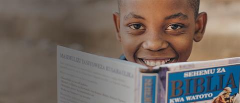 A boy peeks over the top of a Bible he is holding open