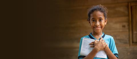 A child smiles and holds letters from a sponsor