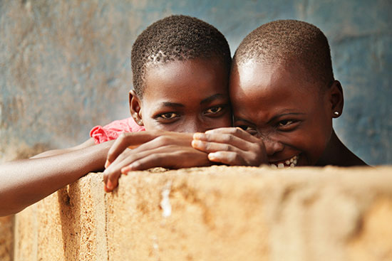 Two Ghanian children peek their eyes over a low cement wall