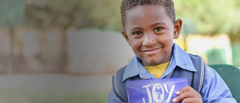 A boy holding a card with the word joy written on it