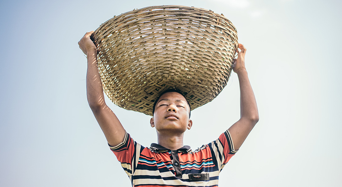 a boy holds a large basket on his head