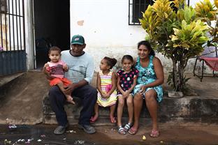 Mycaella and her family sit in front of their home