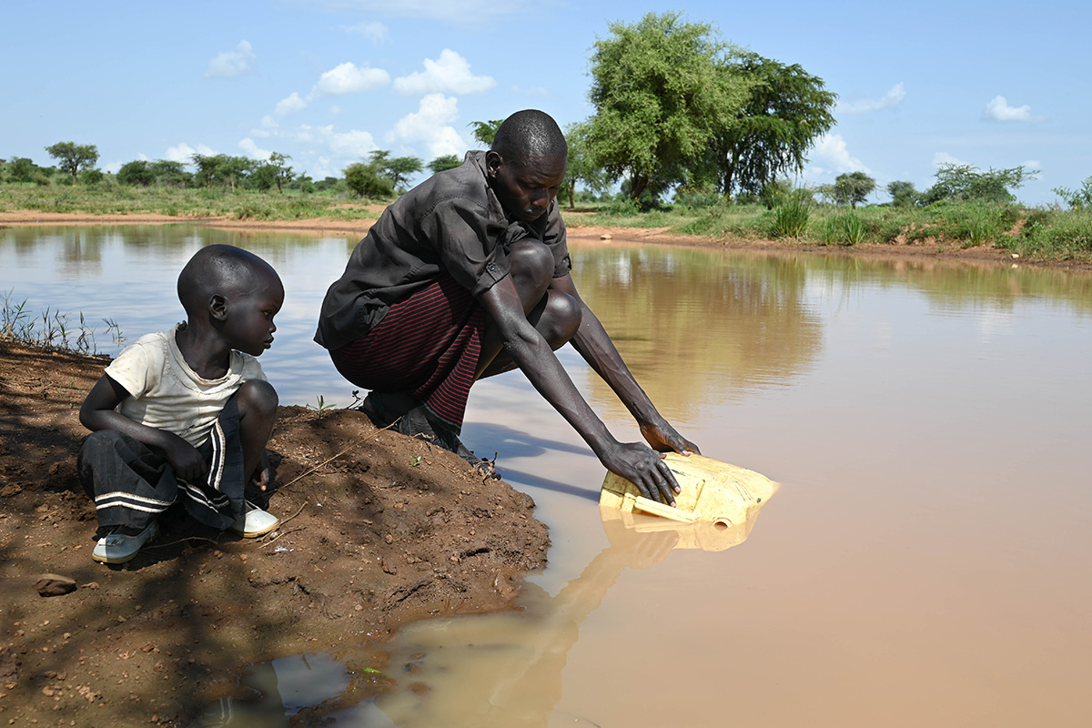 a boy watches his father gather water from a stream