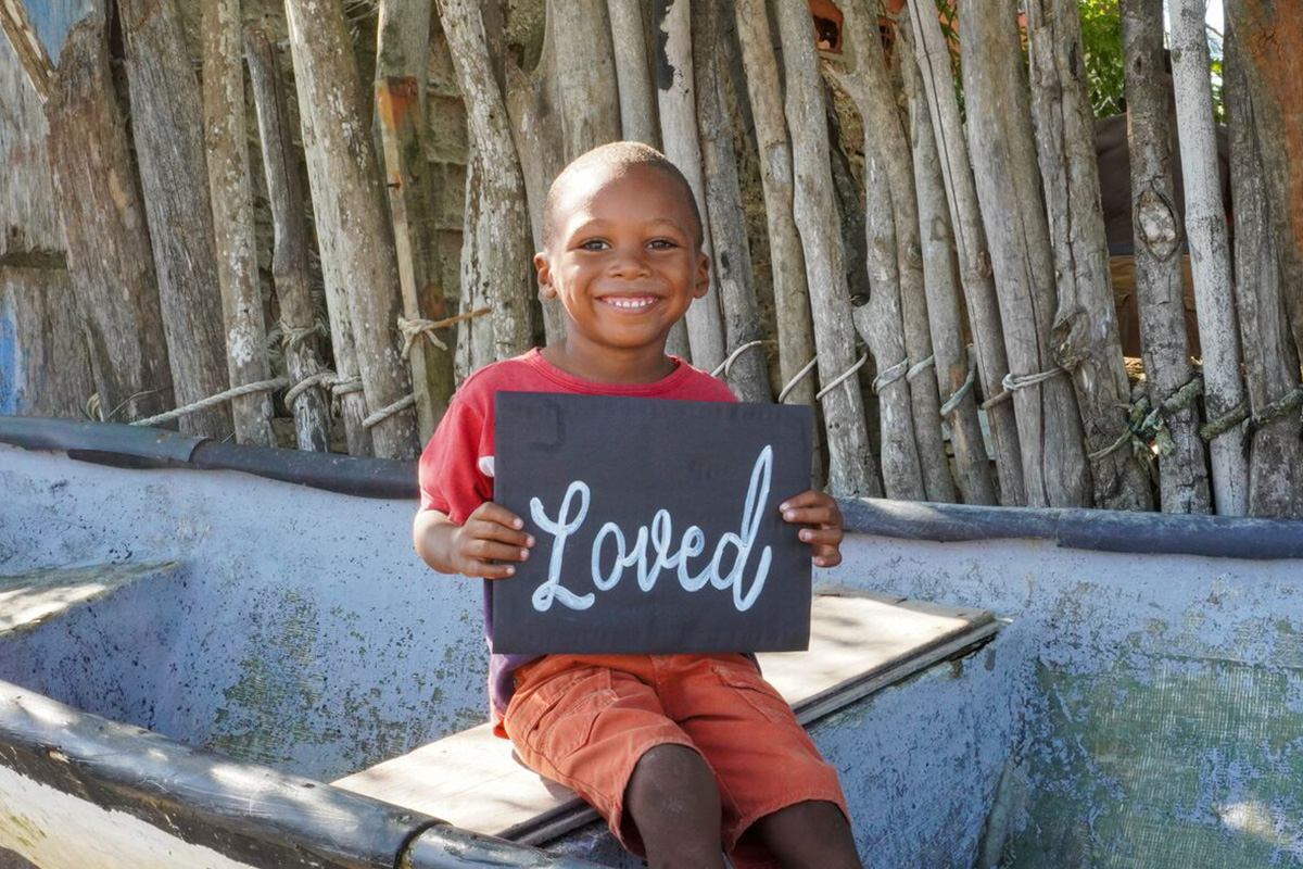 a boy holds a sign that says "Loved"