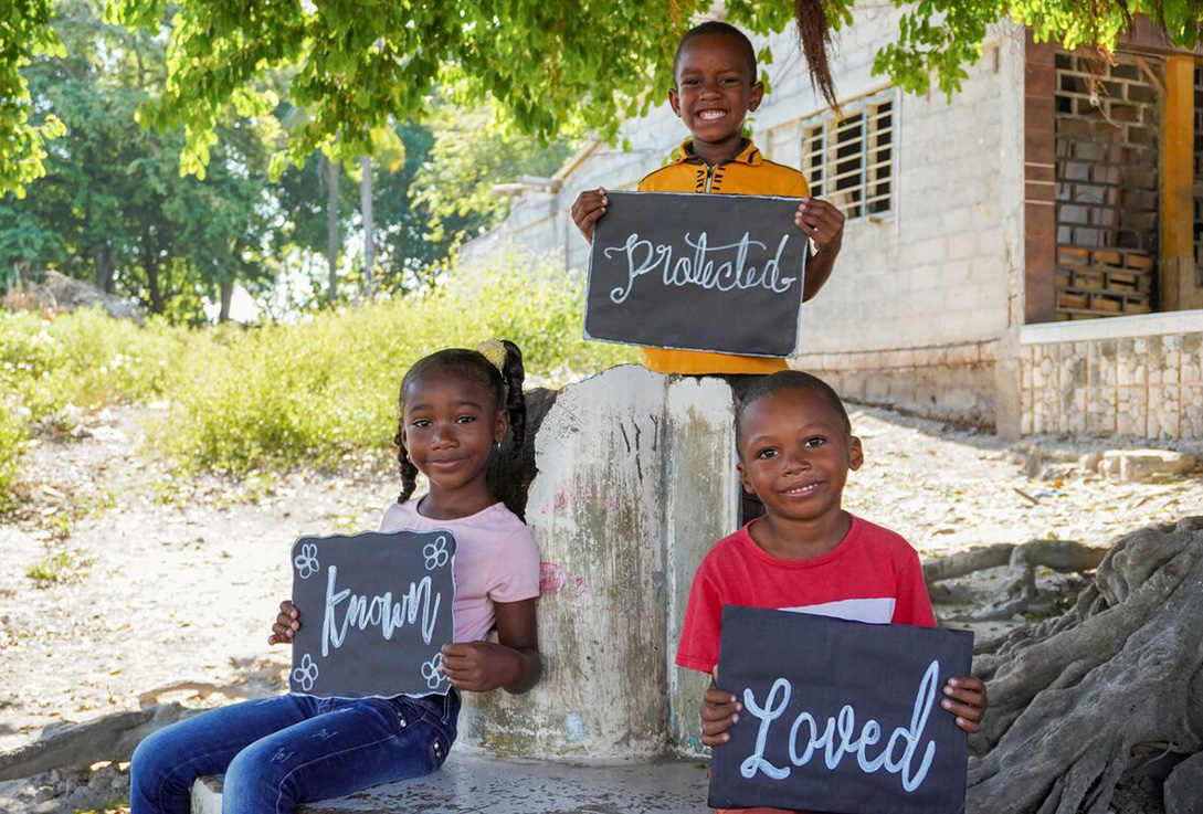 3 children hold signs that say "known", "protected" and "loved"