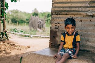 a young boy sits outside his home