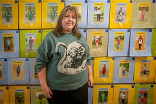 Jenith stands next to a wall of child photos