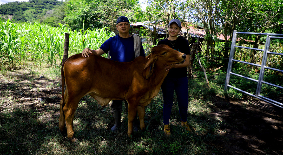 Karina and her father José pose in front of a cow that they recently acquired.