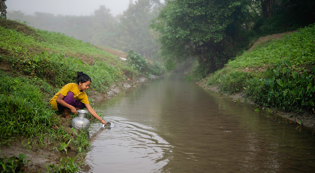 a girl gathers water from a stream