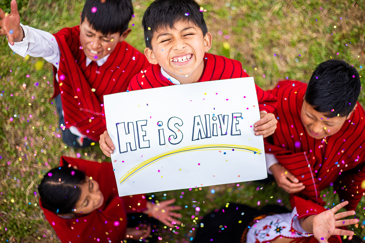 a boy holds a sign that says "He Is Alive"